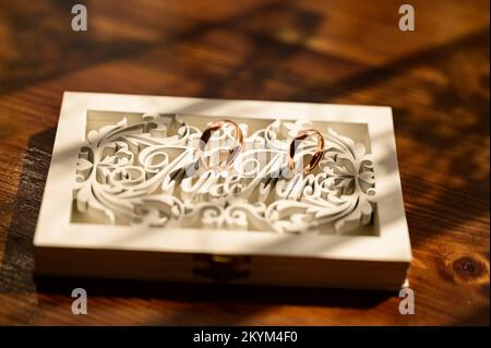 Anelli d'oro di sposi novelli, accessori per matrimoni, anelli close-up, anelli di nozze in una scatola di legno, posto per l'iscrizione. Foto Stock