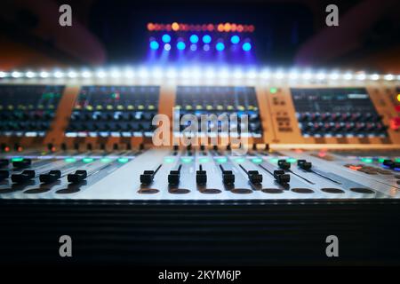 Messa a fuoco selettiva sui cursori della console di mixaggio audio professionale contro i faretti colorati. Foto Stock