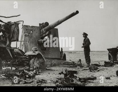 Foto d'epoca circa il 1941 novembre di un ufficiale dell'esercito britannico che esamina il relitto di una pistola d'artiglieria tedesca del 88mm distrutta a Bir el GUBI in Nord Africa durante la seconda guerra mondiale Foto Stock