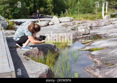 Una donna fotografa le rocce con i petroglifi del Mar Bianco. Zalavruga, complesso archeologico vicino Belomorsk, Carelia, Russia Foto Stock