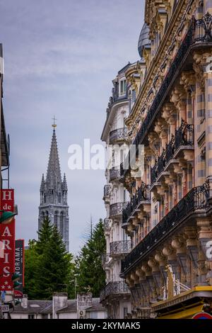 Edificio del 20th ° secolo con la guglia della Basilica di Notre Dame a Lourdes in Francia Foto Stock