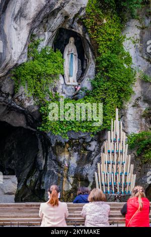 Pellegrini che pregano di fronte alla Grotta di Lourdes con sullo sfondo la statua di Bernadette Soubirous (Francia) Foto Stock