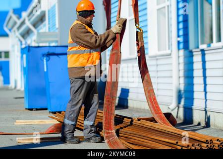 Slinger raccoglie tubi metallici sottili in pila in cantiere. Primo piano. Flusso di lavoro reale. Scarico di materiali per costruzione. Background di produzione per il fornitore di attrezzature.. Foto Stock