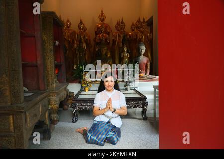 Una signora thailandese in costume thailandese sorride e mette le mani insieme in saluto nella sala di ordinazione buddista Foto Stock
