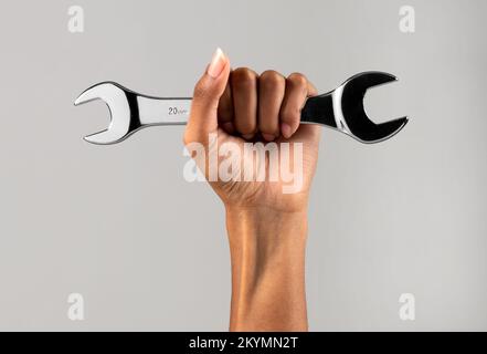 Mano di forte femmina nera serrata a pugno con chiave in metallo contro sfondo grigio Foto Stock