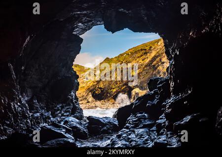 Guardando attraverso la grotta di Merlin per fare surf sulla spiaggia di Tintagel Haven, Tintagel, Cornovaglia, Regno Unito Foto Stock