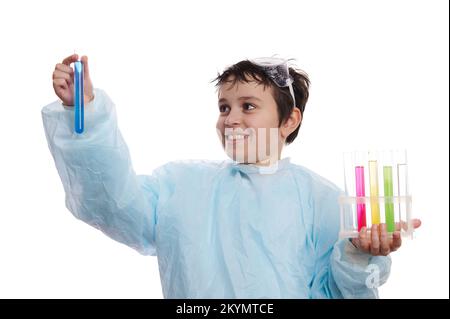 Scolaro intelligente in uniforme da laboratorio, ispezionando la reazione chimica in provette isolate su fondo bianco Foto Stock