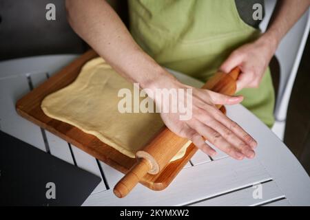 Concetto di pasticceria di Pasqua. Cuoco caucasico maschio panettiere in grembiule verde preparazione di pasta in cucina impastare un impasto su un tagliere di legno utilizzando un matterello. Immagini di alta qualità Foto Stock