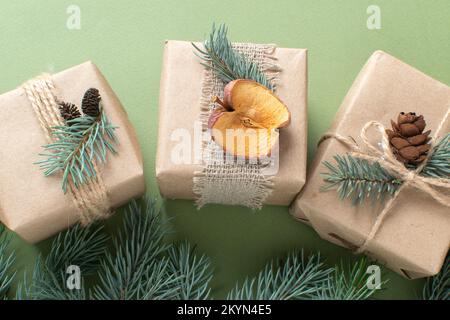 Tre regali di Natale avvolti in carta kraft e dipinti con materiali naturali, su sfondo verde, Natale senza sprechi. Fatelo da soli. Spazio Foto Stock