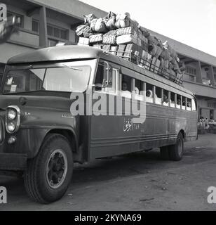 1960s, storico, parcheggiato all'esterno di un autobus importato American International Harvester serie B, con i passeggeri seduti all'interno e un ampio bagaglio e carico caricato sul tetto, legato con corda, Riyadh, Arabia Saudita. Foto Stock