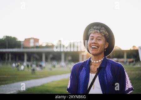 Ritratto di giovane allegro con capelli ricci che indossano cappello al parco Foto Stock