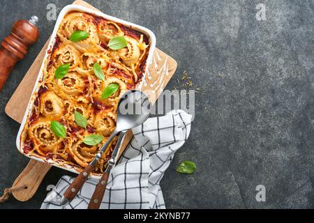 Lasagne. Lasagne fatte in casa - rotolo di pasta cuocere con salsa di pomodoro, crema di formaggio e basilico su padella bianca su fondo di ardesia scura, pietra o cemento. Esso Foto Stock