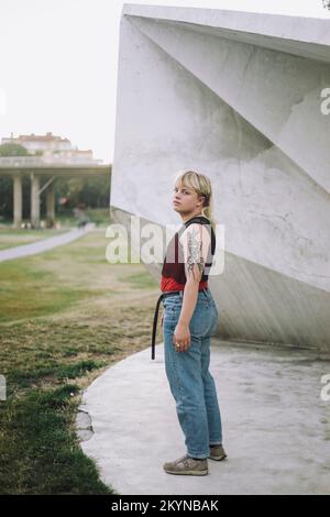 Vista laterale di una persona non binaria in piedi vicino alle mura del parco Foto Stock