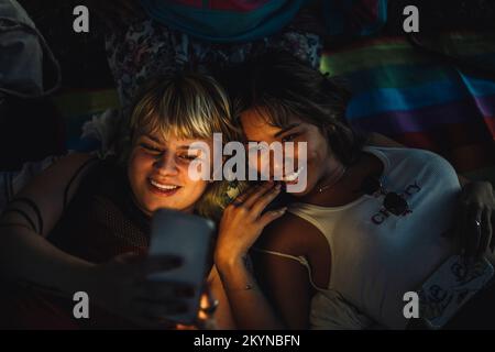 Felice non-binary persona che prende selfie con l'amico femmina attraverso lo smartphone Foto Stock