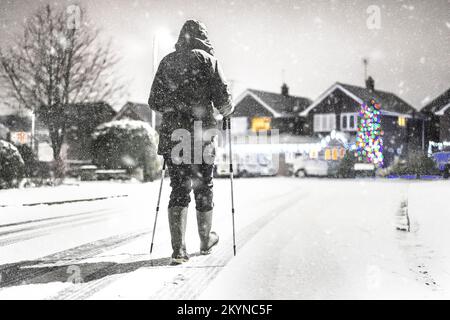Vista posteriore della donna in giacca invernale, cappuccio su, camminando isolato lungo una strada residenziale a Natale con bastoni in caduta di neve. Foto Stock