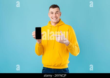 Entusiasta simpatico ragazzo caucasico che dimostra lo smartphone con schermo nero vuoto e che punta su di esso, mockup Foto Stock