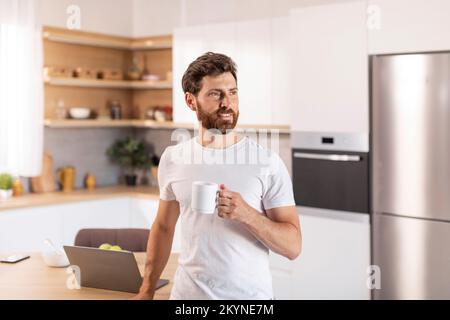 Sorridente uomo caucasico maturo con barba in t-shirt bianca pensa, ama bere in tazza, guarda lo spazio libero Foto Stock