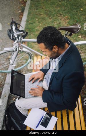 Professionista che utilizza il computer portatile mentre si siede sulla panca Foto Stock