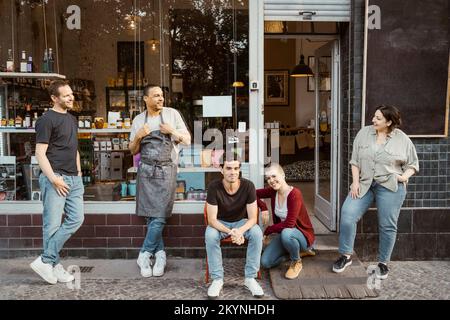 Proprietari di negozi multirazziali che parlano l'uno con l'altro al di fuori deli Foto Stock