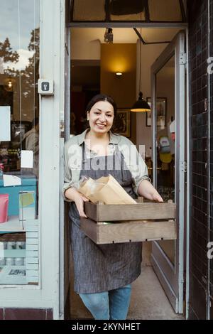 Ritratto di felice proprietario femmina in piedi alla porta di deli gabbia di tenuta Foto Stock