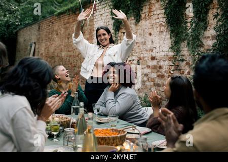 Donna sorridente gesturing mentre godendo con gli amici durante la festa della cena nel cortile posteriore Foto Stock