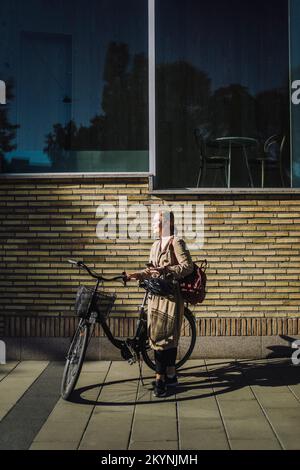 Donna d'affari con bicicletta in piedi davanti al muro Foto Stock