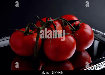 un ramo di pomodori su sfondo a specchio, in un primo piano scuro, fuoco selettivo, riflesso in un vassoio Foto Stock