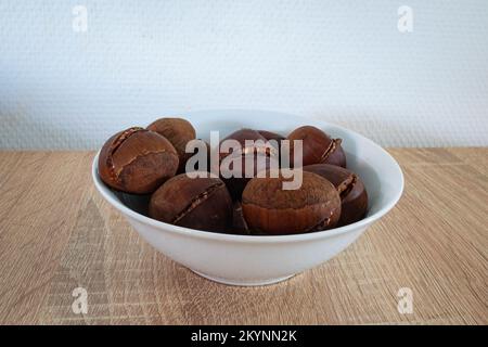 Ciotola con castagne arrostite su fondo bianco Foto Stock