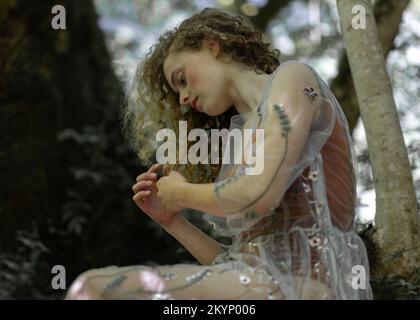 Bella ragazza con lunghi capelli ricci siede su un albero Foto Stock