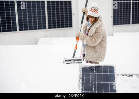 La donna pulisce i pannelli solari dalla neve Foto Stock