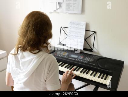 Donna che suona pianoforte elettrico da spartiti musicali Foto Stock