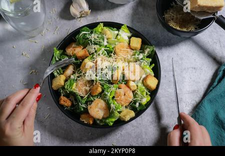 Primo piano di una donna che mangia insalata Cesar con forchetta sul tavolo di marmo grigio Foto Stock