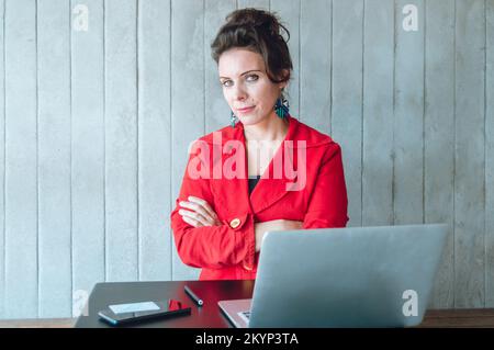 serio business caucasico verde occhio donna adulta con le braccia incrociate seduta con il suo computer portatile in un bar guardando la fotocamera Foto Stock