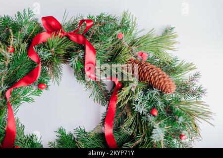 Corona di Natale e Capodanno in abete, rami sempreverdi abete rosso pino, fianchi di rose, coni decorati con arco a nastro rosso su sfondo bianco. Foto Stock
