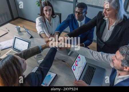 Uomini d'affari multirazziali giovani e anziani motivati e felici che si uniscono ai pugni, mostrando sostegno e spirito di squadra insieme, celebrando l'azienda Foto Stock