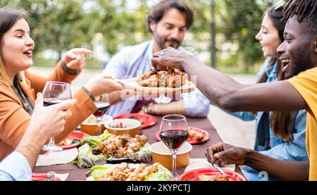 Gruppo di amici multietnici che pranzano al tavolo della fattoria - diversi giovani seduti a casa durante la festa barbecue Foto Stock