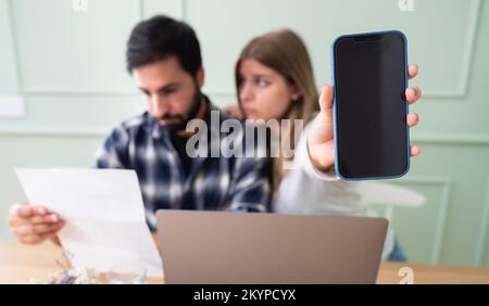 Giovane coppia sposata spaventato dai conti in aumento. Primo piano della mano di una ragazza giovane che tiene uno smartphone con sfondo è sfocato.Mockup. Foto Stock