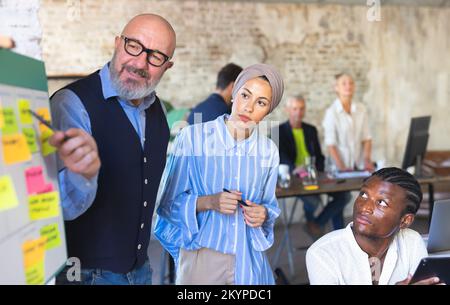 Gruppo di team multirazziali che si riunisce in un ufficio moderno e analizza i dati insieme. Integrazione del personale aziendale e concetto di startup Foto Stock