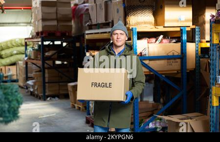 Addetto al magazzino che trasporta grandi scatole di merci in arehouse Foto Stock