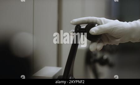 Vista ravvicinata della mano in un guanto protettivo bianco che ruota l'ampia maniglia nera di un contenitore o di un contenitore in metallo. Manopola e maniglia della porta del vault Foto Stock