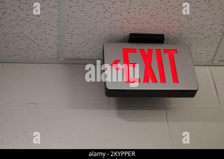 Cartello d'uscita nell'edificio scolastico degli Stati Uniti con pareti dipinte e soffitto a discesa. Le parole EXIT sono illuminate in rosso brillante con una freccia direzionale rivolta verso sinistra. Foto Stock