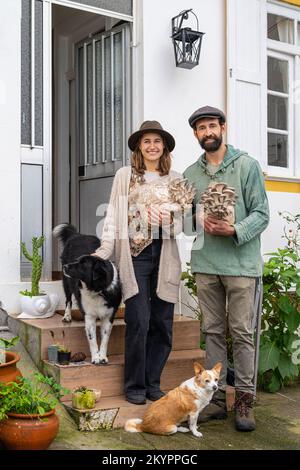 Giovane coppia che tiene blocchi di funghi ostriche vicino casa Foto Stock