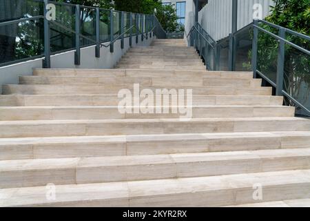 Ampie scale all'aperto con balaustra in vetro e corrimano in metallo a Miami, Florida. Scale con mattonelle di struttura di legno vicino alle piante, agli alberi e all'edificio Foto Stock