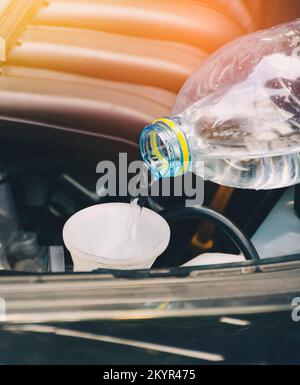 Il meccanico auto sta versando acqua pulita nel serbatoio di un sistema di tergicristallo auto, concetto di servizio di manutenzione automobilistica Foto Stock