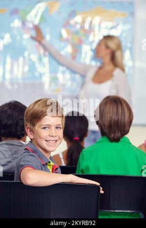 Ama imparare cose nuove sul mondo. Ritratto di un ragazzino seduto con i compagni di classe durante una lezione di geografia. Foto Stock