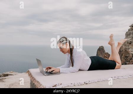 Silhouette di computer portatile e tazza sulla spiaggia sul tramonto del mare. Acqua di mare frizzante sullo sfondo. Freelance, blogger che lavora su notebook in spiaggia. Foto Stock