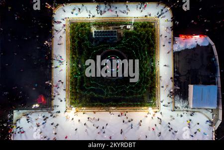 Bellissimo paesaggio urbano. Molte persone pattinano su una pista di pattinaggio all'aperto con illuminazione e ghirlande la sera d'inverno nel parco pubblico della città. Drone aereo Visualizza sfondo. Luci di Natale di Capodanno Foto Stock