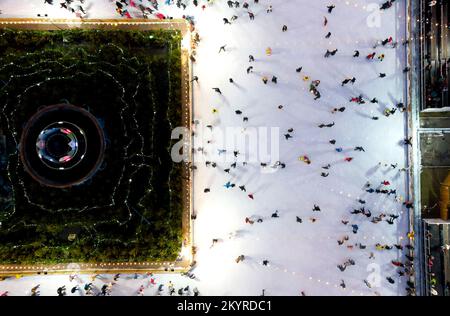 Bellissimo paesaggio urbano. Molte persone pattinano su una pista di pattinaggio all'aperto con illuminazione e ghirlande la sera d'inverno nel parco pubblico della città. Drone aereo Visualizza sfondo. Luci di Natale di Capodanno Foto Stock