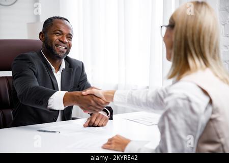 Assunzione, colloquio. Business african american boss di mezza età che ha un colloquio di lavoro in un ufficio luminoso. Guarda il curriculum e dopo averlo letto Foto Stock