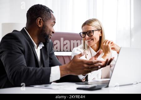 Due persone analizzano i documenti su un notebook mentre sono seduti a un tavolo in ufficio. I partner commerciali al lavoro in ufficio stanno discutendo i progetti Foto Stock